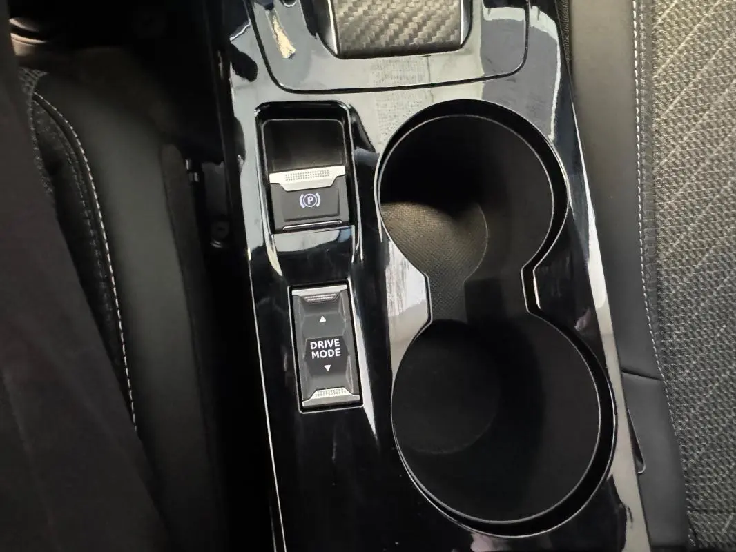 Gros plan sur la console centrale noire du Peugeot 2008 Hybrid 145 Allure, avec boutons frein à main et mode de conduite.