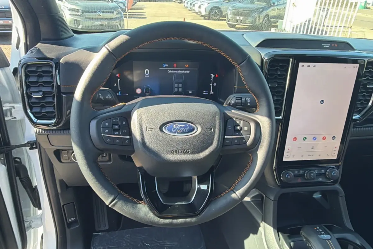 Vue intérieure frontale du volant cuir noir avec surpiqûres marron du Ford Ranger blanc, écran tactile vertical et tableau de bord digital.