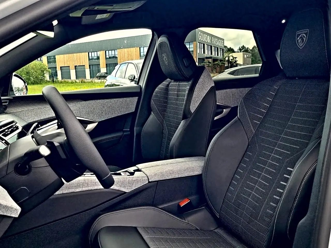 Intérieur avant droit du Peugeot 3008 2026, sièges tissu noir avec logo Peugeot brodé sur appuie-tête.