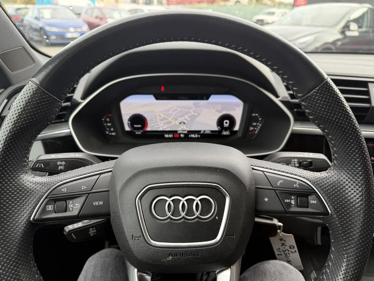 Vue rapprochée du volant en cuir noir perforé et du tableau de bord numérique d'un Audi Q3 Quattro 2019.
