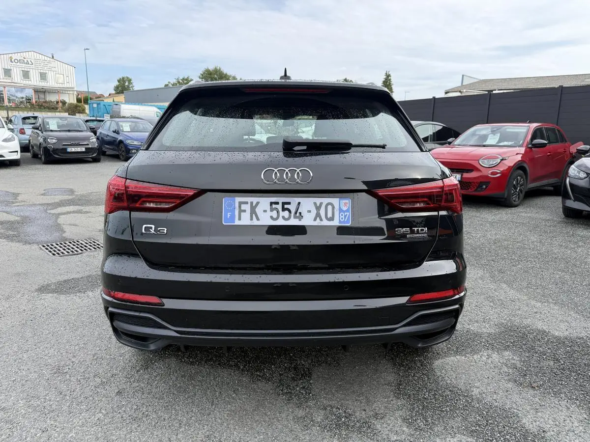 Vue arrière d'un Audi Q3 noir 2019 avec badges Quattro et 35 TDI, stationné sur un parking humide.
