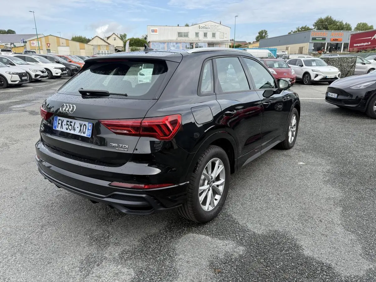 Audi Q3 noir vue 3/4 arrière droit sur parking, avec feux arrière LED et jantes aluminium 5 branches.