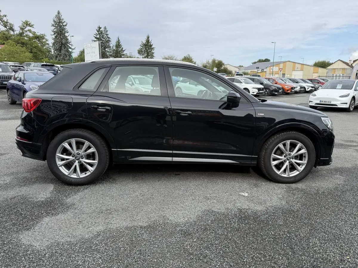 Audi Q3 S Line noire vue de profil côté gauche sur un parking avec jantes en aluminium et vitres légèrement teintées.