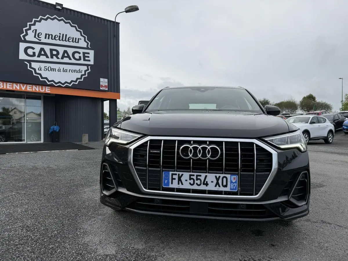 Audi Q3 Quattro S Line noire vue de face avec calandre chromée et phares LED allumés sur parking devant garage.