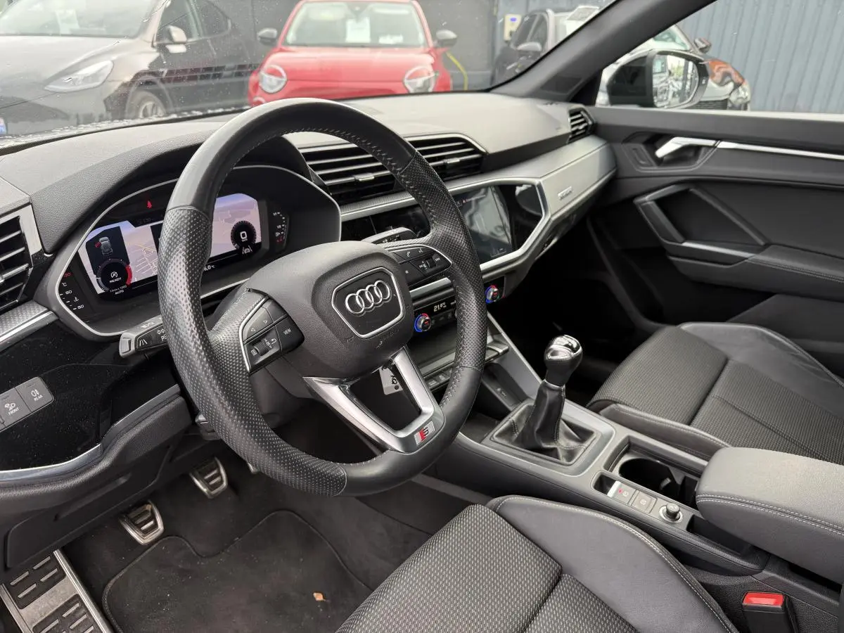 Intérieur noir de l'Audi Q3 S Line 2019, vue côté conducteur sur volant, levier manuel et tableau de bord numérique.