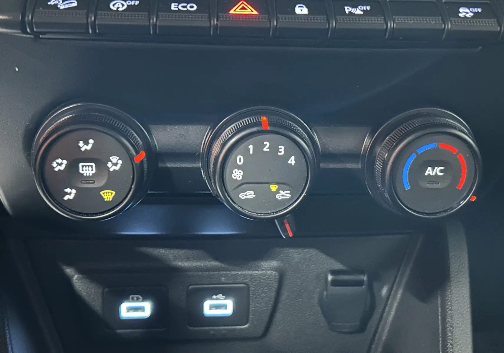 Gros plan sur les commandes de climatisation et les ports USB du tableau de bord du Dacia Duster blanc 2023.