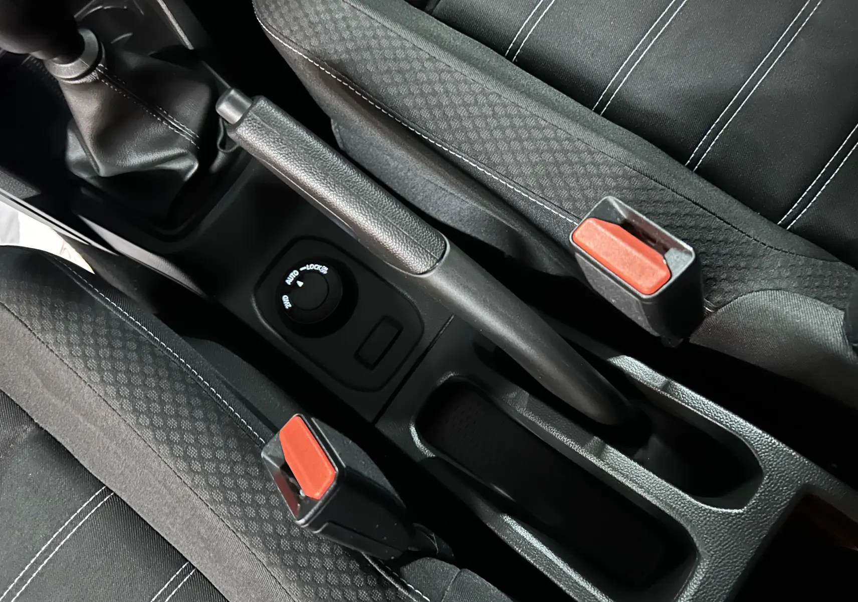 Vue rapprochée de la console centrale du Dacia Duster 2023, montrant frein à main et sièges tissu noirs avec surpiqûres blanches.
