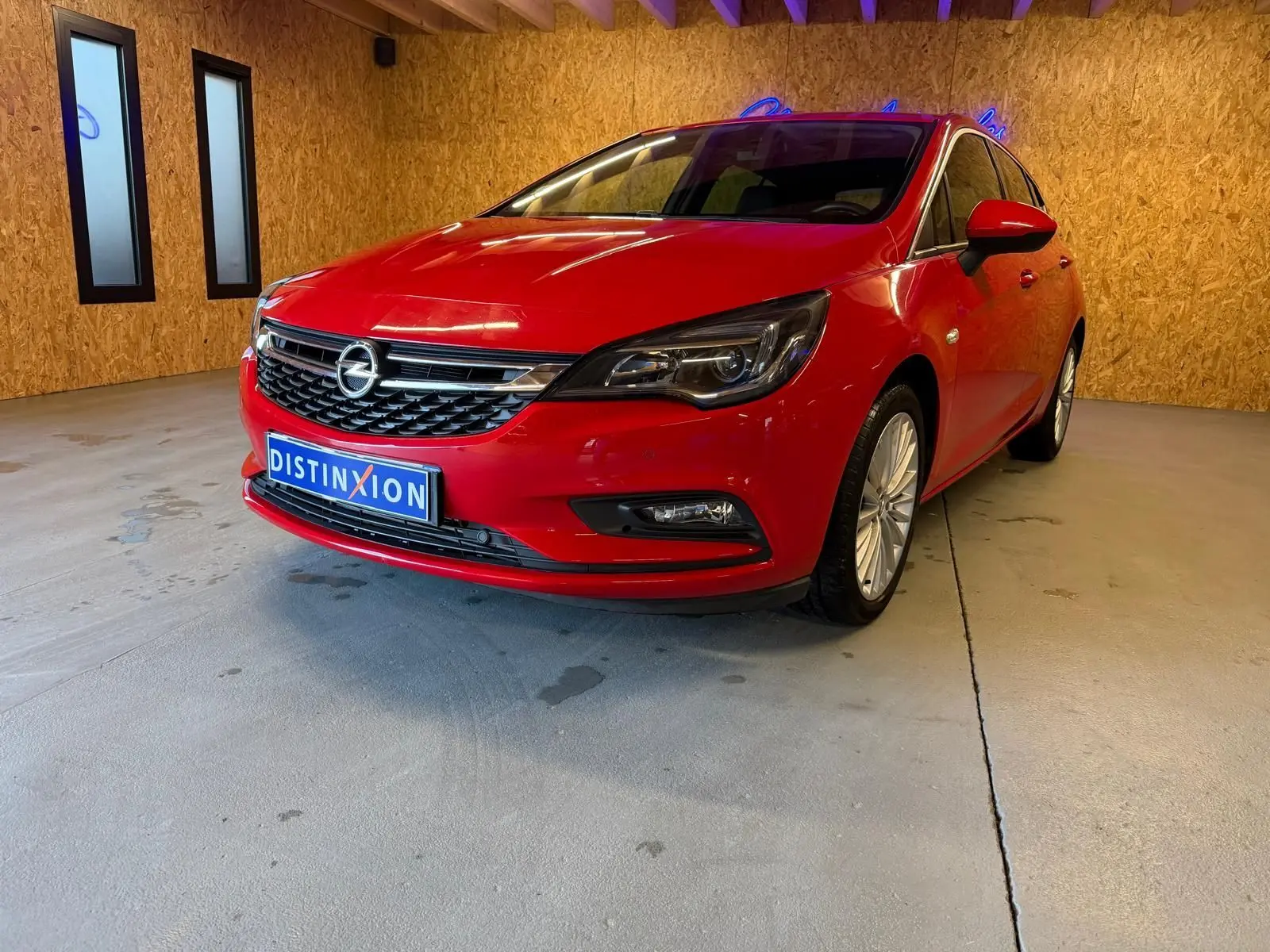Vue 3/4 avant droite d'une Opel Astra rouge 2016 avec jantes alu et phares halogènes dans un garage.