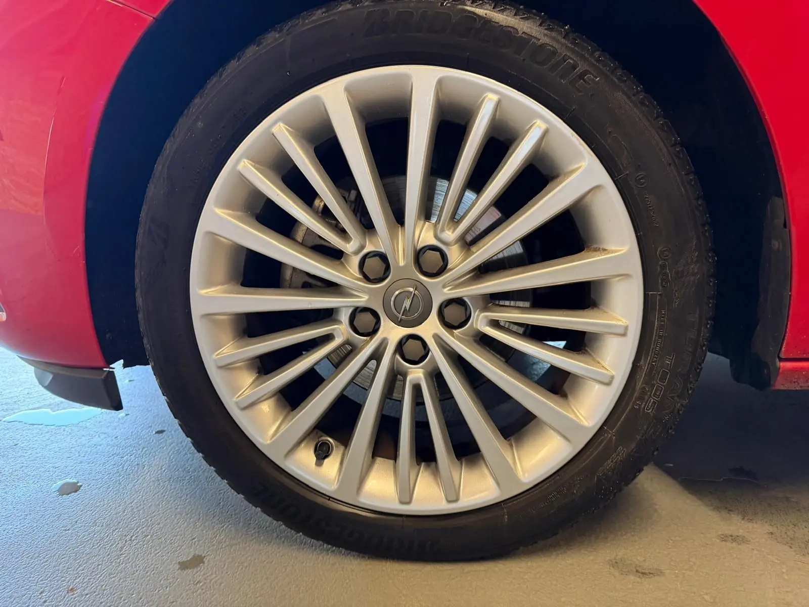 Gros plan sur la jante alu argentée d'une Opel Astra rouge, mettant en valeur le logo central et le pneu Bridgestone.