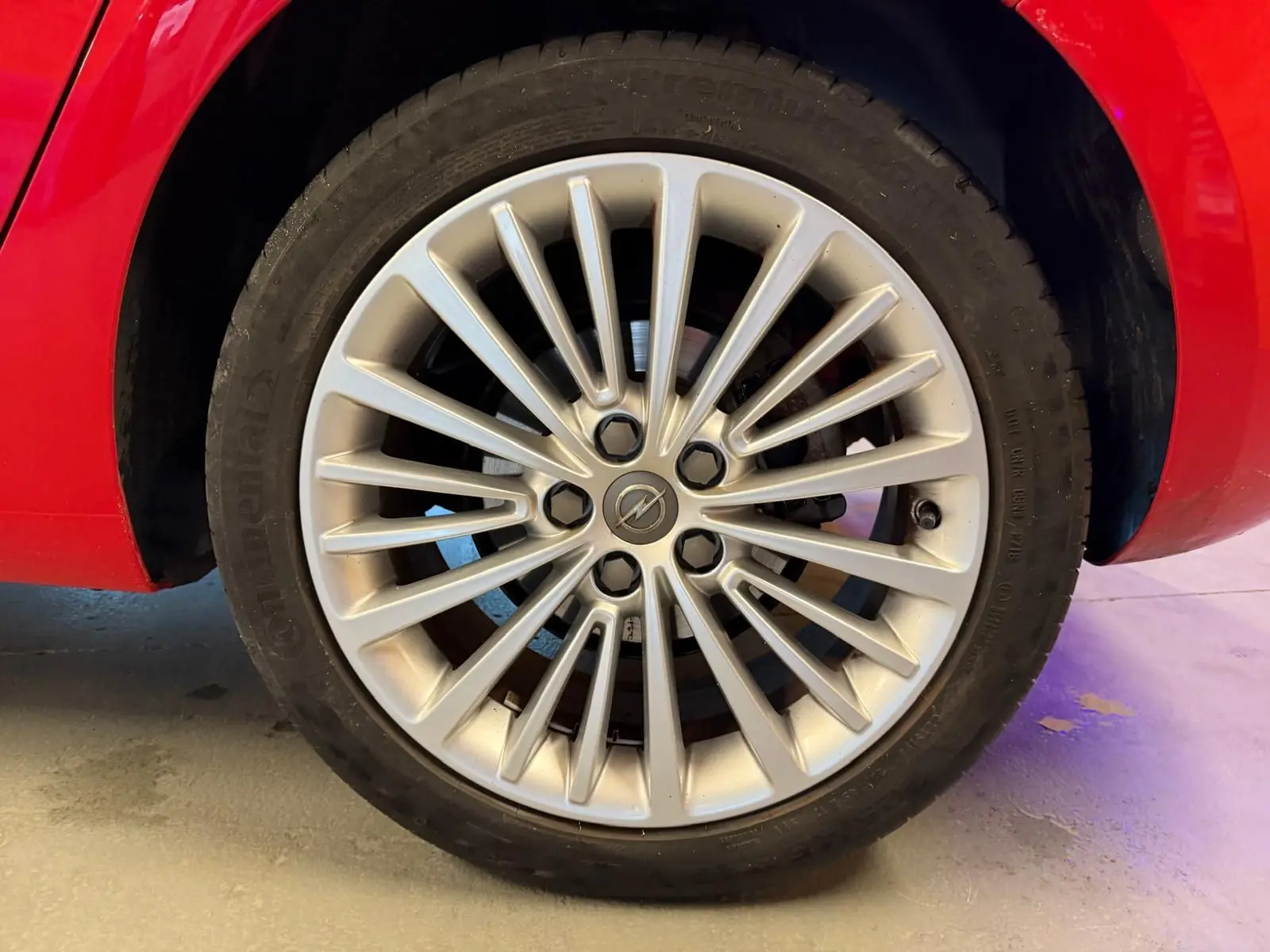 Gros plan sur la jante alu argentée d'une Opel Astra rouge, mettant en valeur le logo central Opel.
