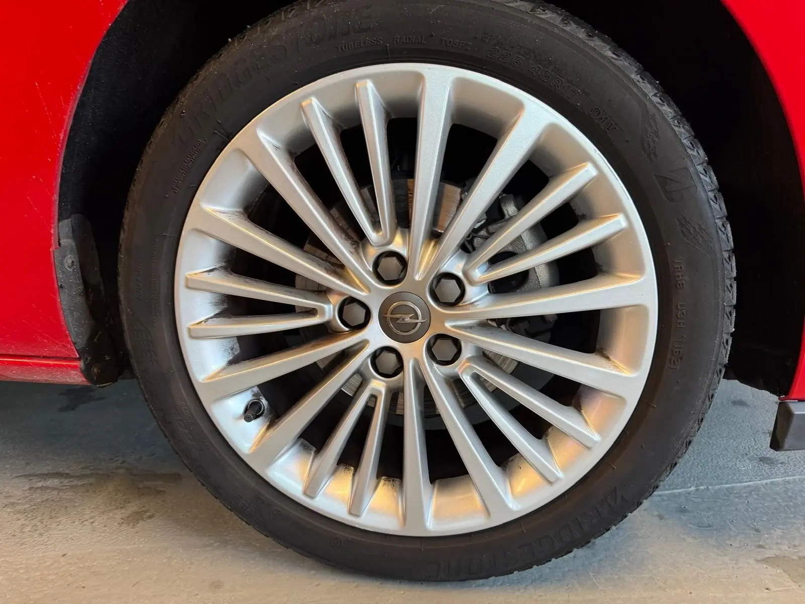 Gros plan sur la jante alu argentée et le pneu Bridgestone d'une Opel Astra rouge, côté avant gauche.