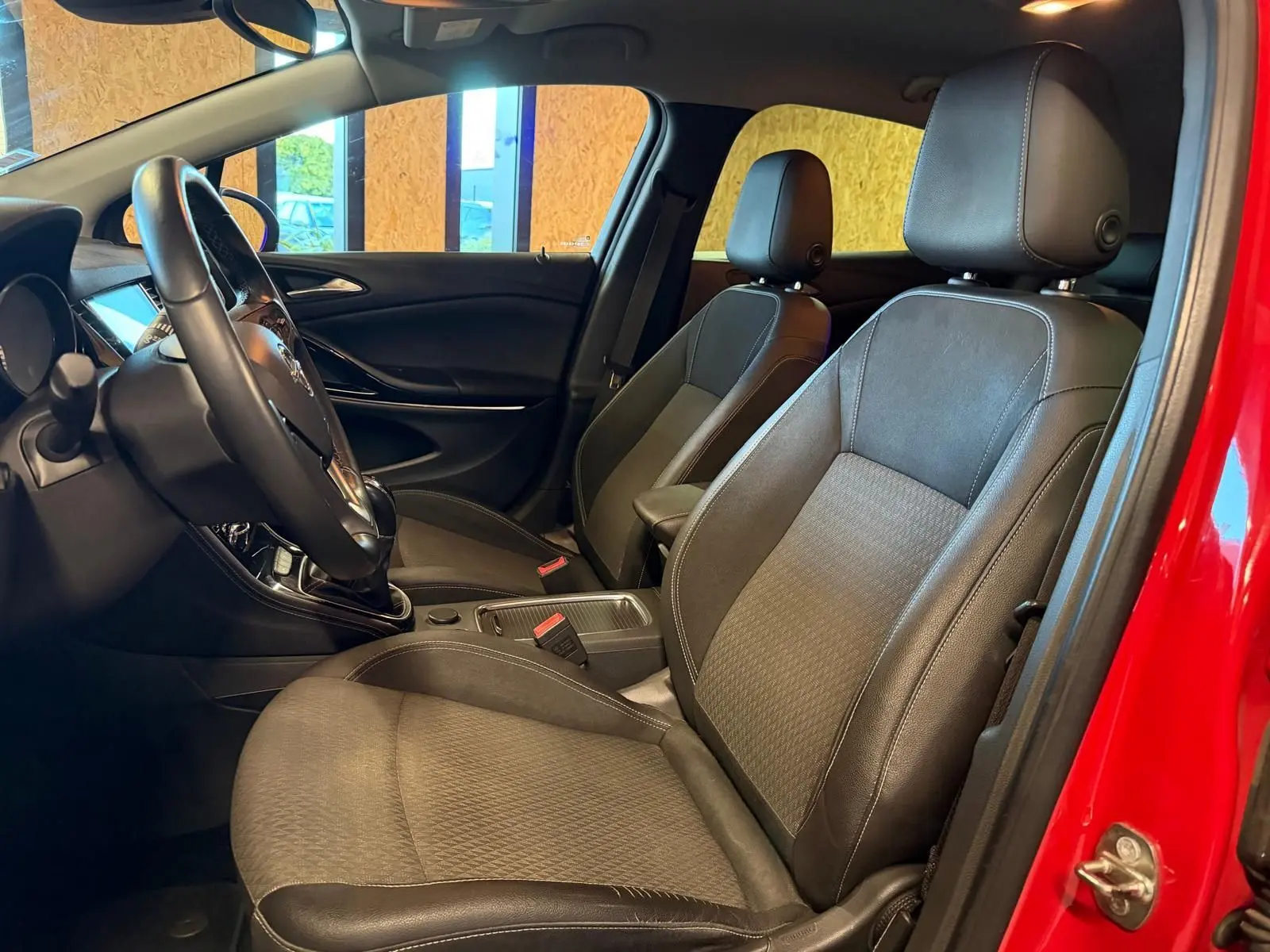 Intérieur avant de l’Opel Astra rouge, vue côté conducteur montrant sièges tissu et cuir noirs avec volant multifonctions.