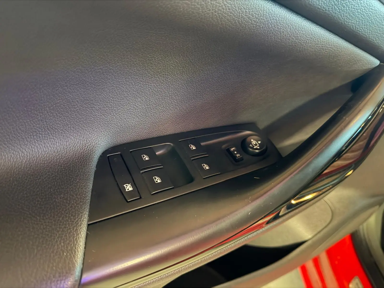 Gros plan sur les commandes de vitres et rétroviseurs côté conducteur d'une Opel Astra rouge.