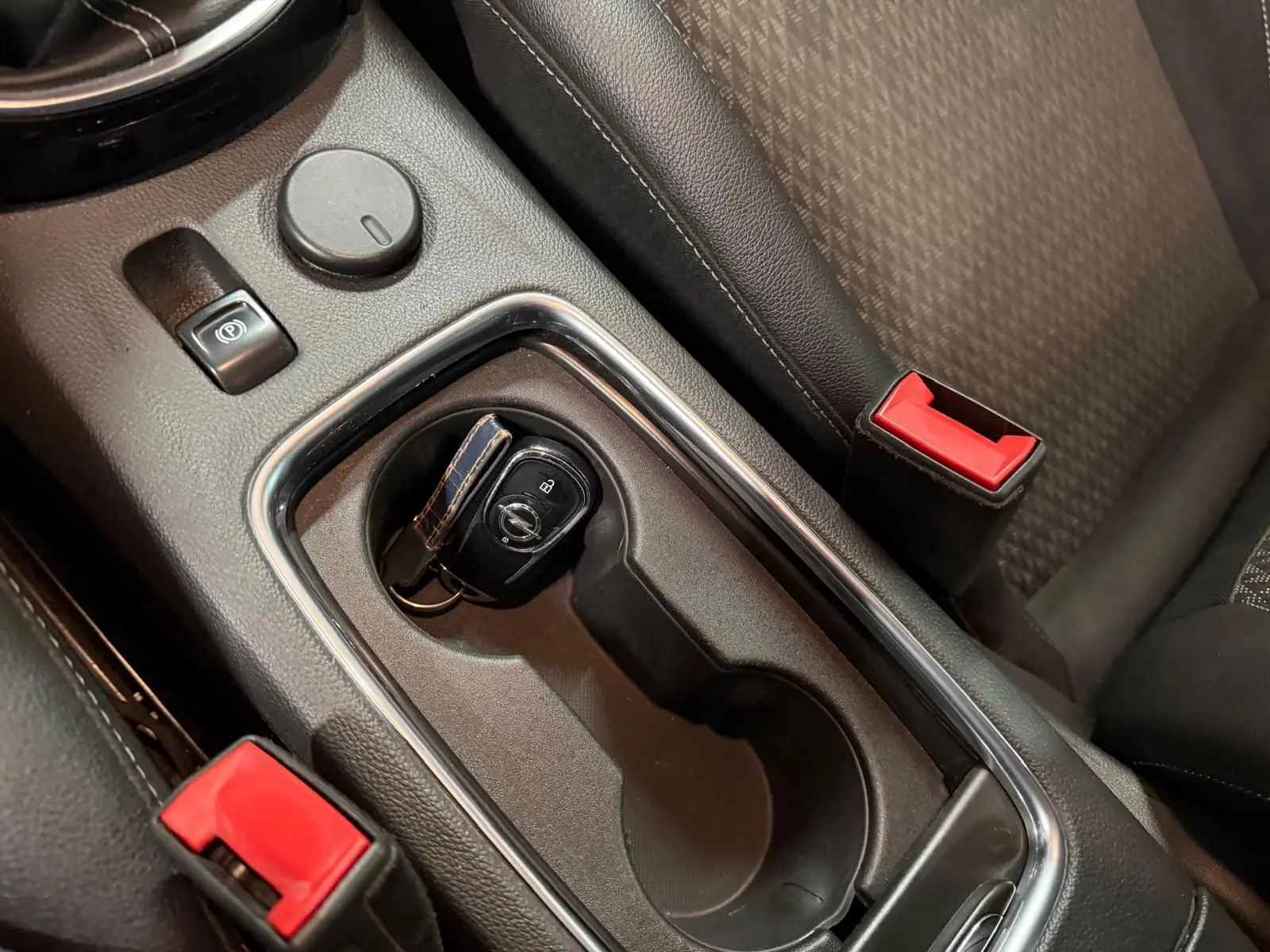 Vue rapprochée de la console centrale intérieure de l'Opel Astra 2016 avec clé, frein à main électrique et ceintures rouges.