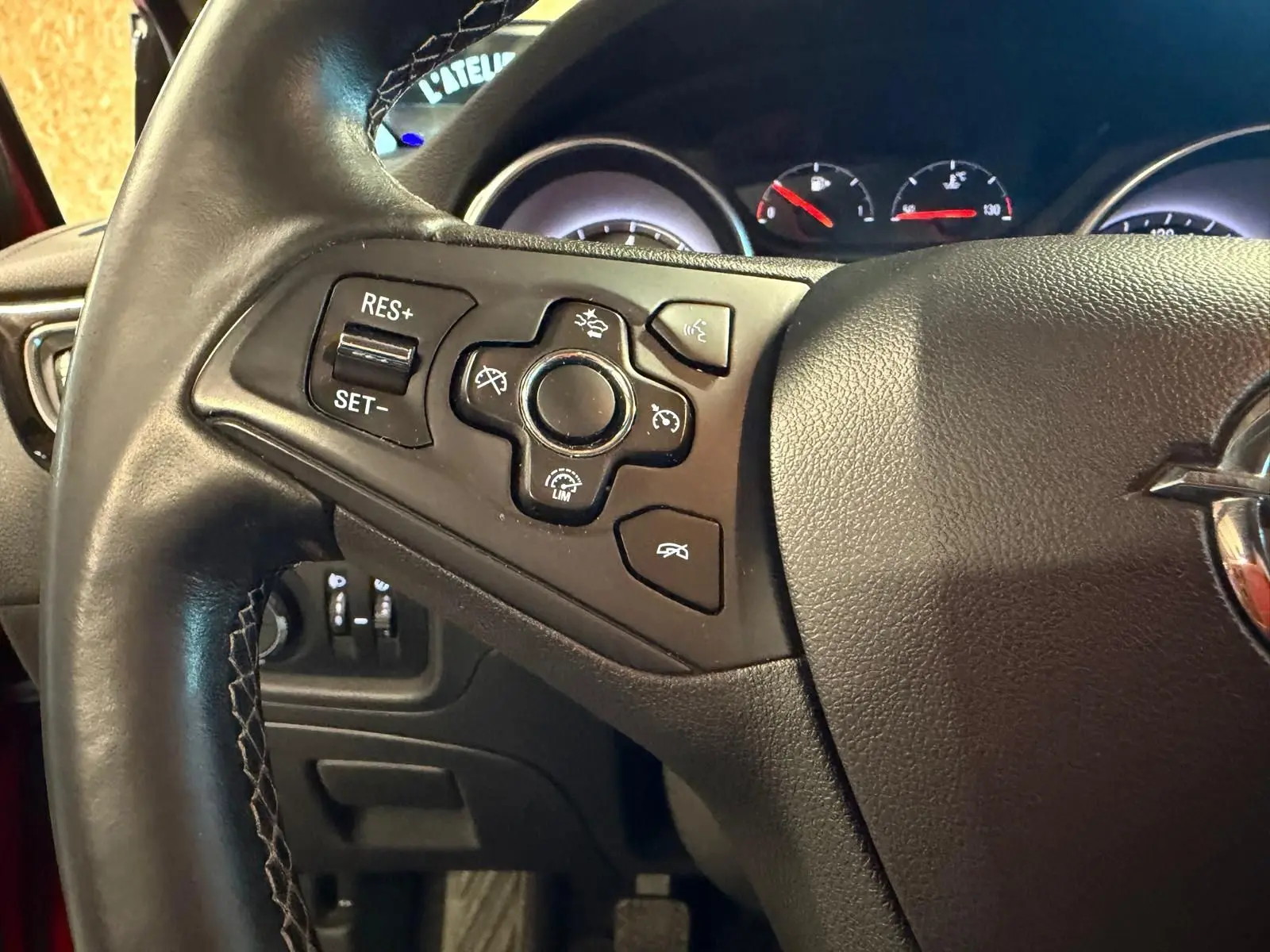 Gros plan sur le volant cuir multifonctions noir d’une Opel Astra rouge, avec commandes de régulateur de vitesse.