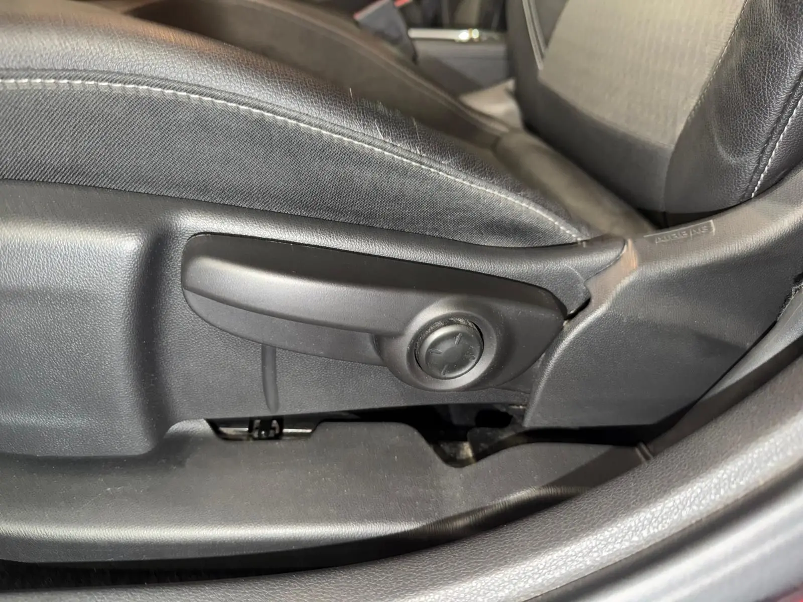 Détail du réglage manuel du siège avant en cuir noir de l'Opel Astra 1.4i Turbo rouge, côté conducteur.