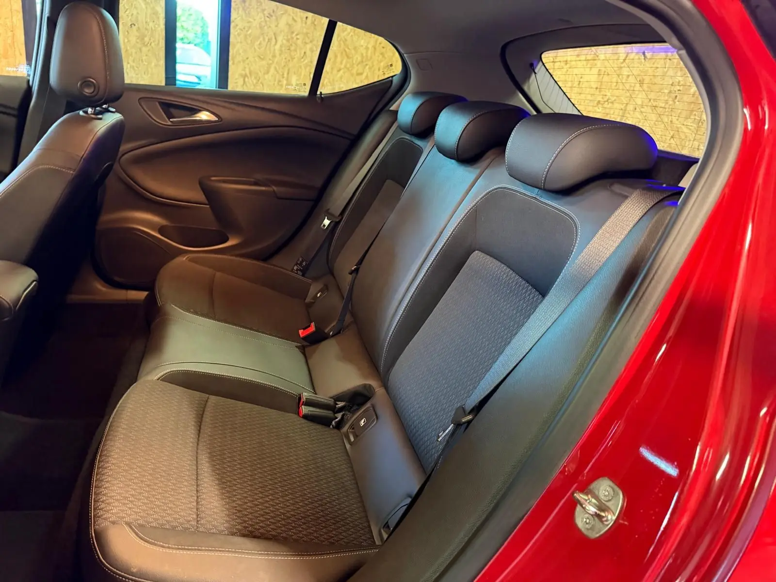 Vue intérieure côté droit arrière de l’Opel Astra rouge, montrant la banquette arrière en tissu et cuir avec appuis-têtes.
