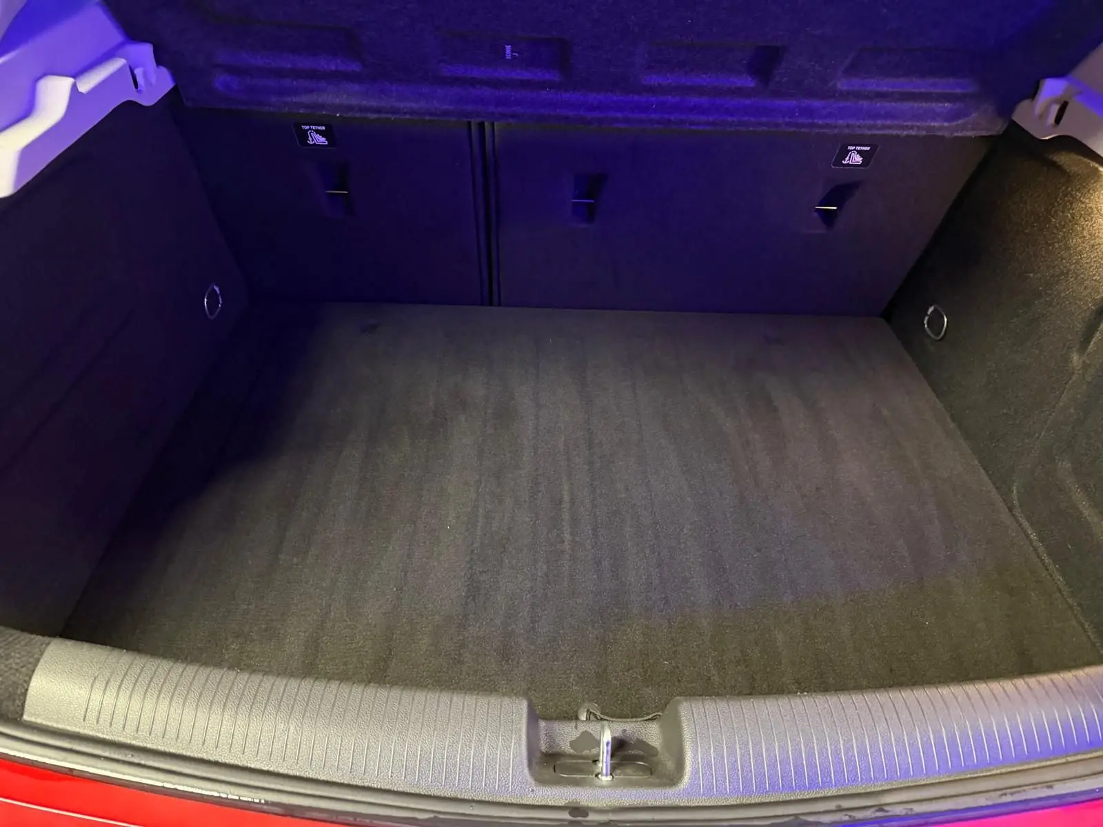 Coffre ouvert vu de face, intérieur noir, bord de carrosserie rouge visible en bas.