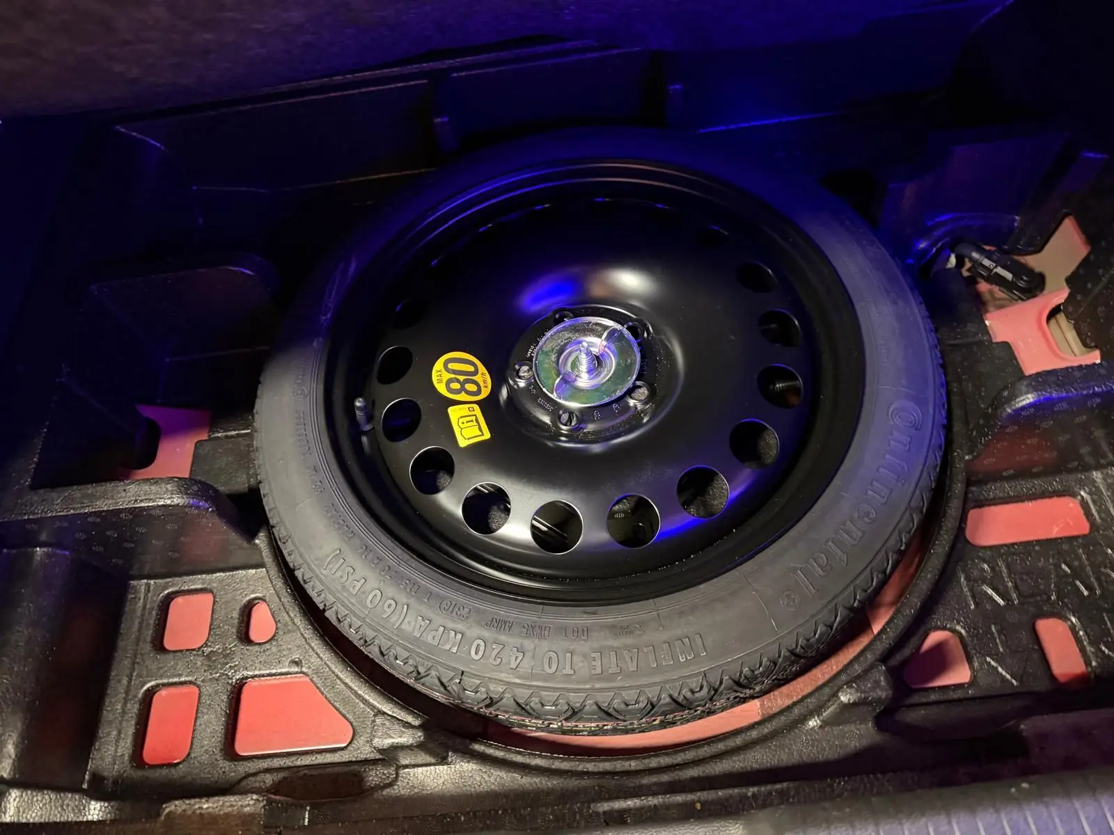 Vue rapprochée de la roue de secours noire dans le coffre d'une Opel Astra rouge 2016.