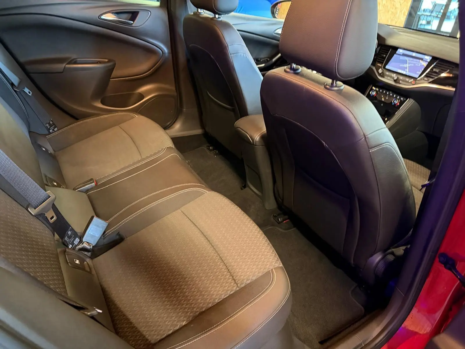 Vue intérieure arrière droite de l’Opel Astra rouge, montrant la banquette tissu et les sièges avant en cuir noir.