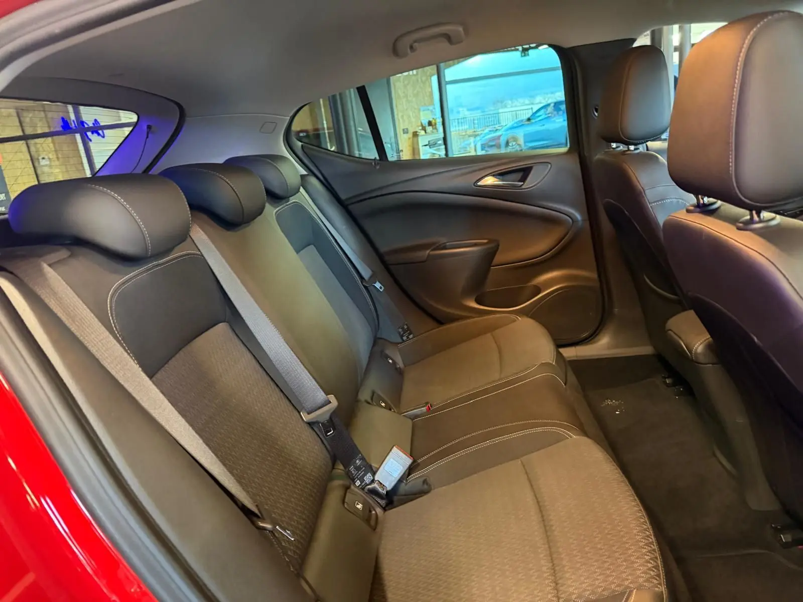Vue intérieure arrière de l’Opel Astra rouge, montrant la banquette arrière en tissu avec appuis-têtes et ceintures de sécurité.