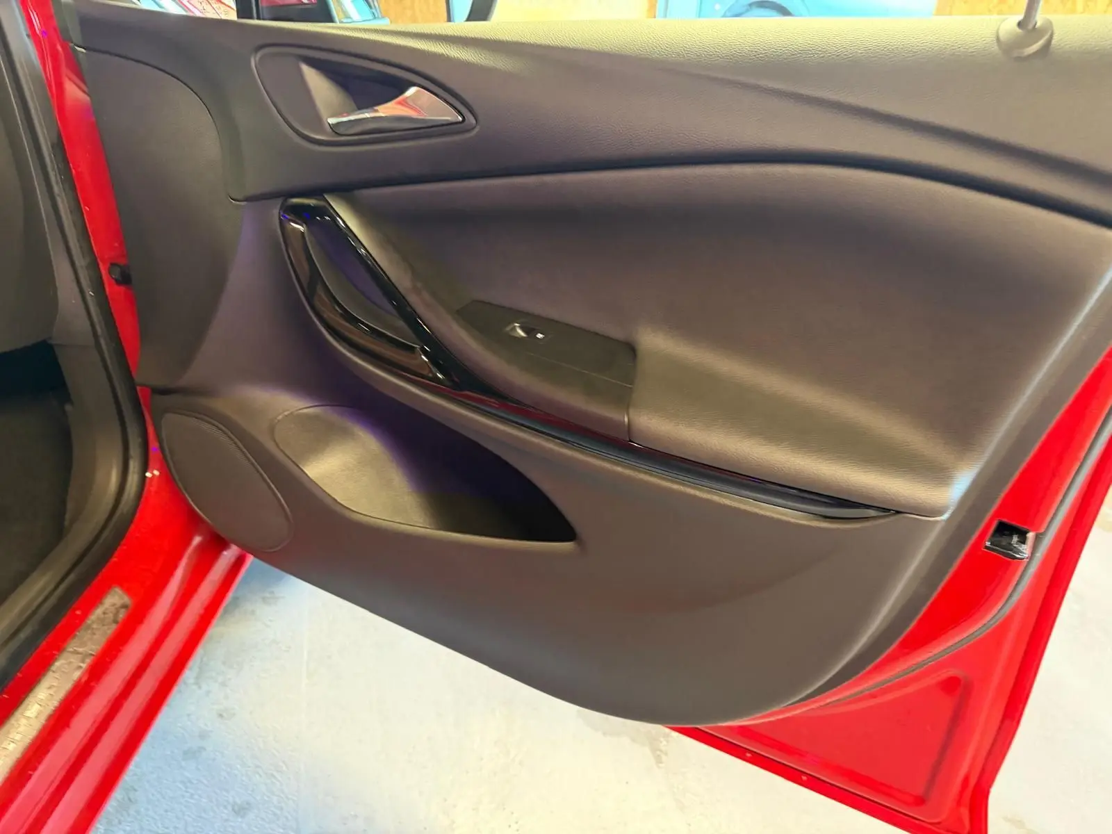 Vue rapprochée de la porte avant gauche rouge d'une Opel Astra 2016 avec garniture intérieure noire et poignée brillante.