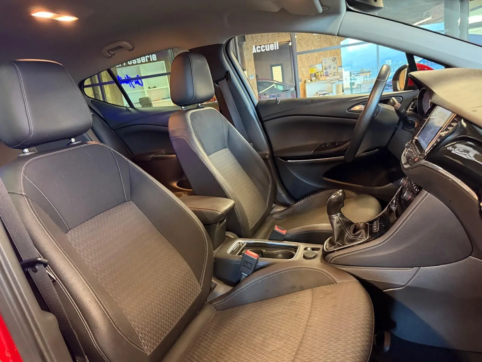 Vue intérieure côté droit de l’Opel Astra rouge 2016, montrant sièges avant, volant cuir et écran tactile.