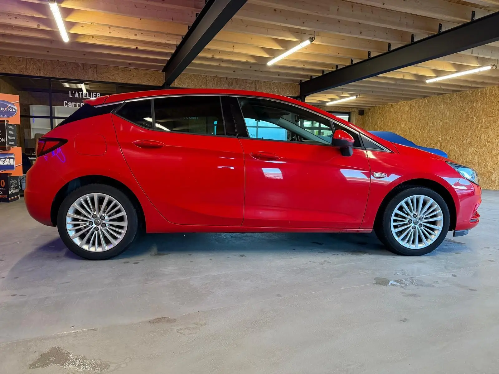 Opel Astra rouge vue de profil côté gauche, jantes alliage et rétroviseurs électriques rabattables visibles.