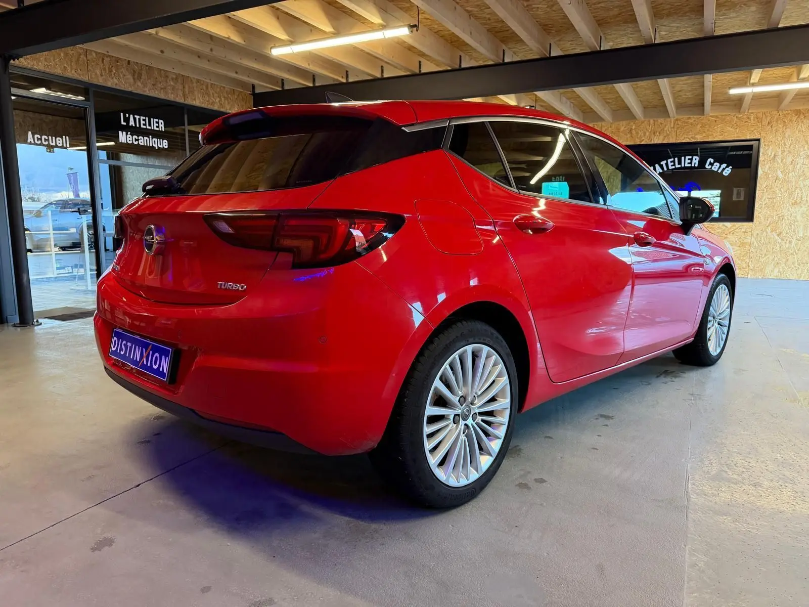Vue 3/4 arrière droite d'une Opel Astra rouge 2016 avec jantes alu et vitres teintées dans un garage.