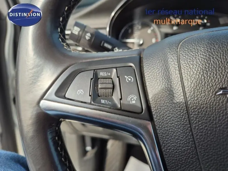 Gros plan sur les commandes du régulateur de vitesse au volant cuir noir d'un Opel Mokka X gris Minéral.