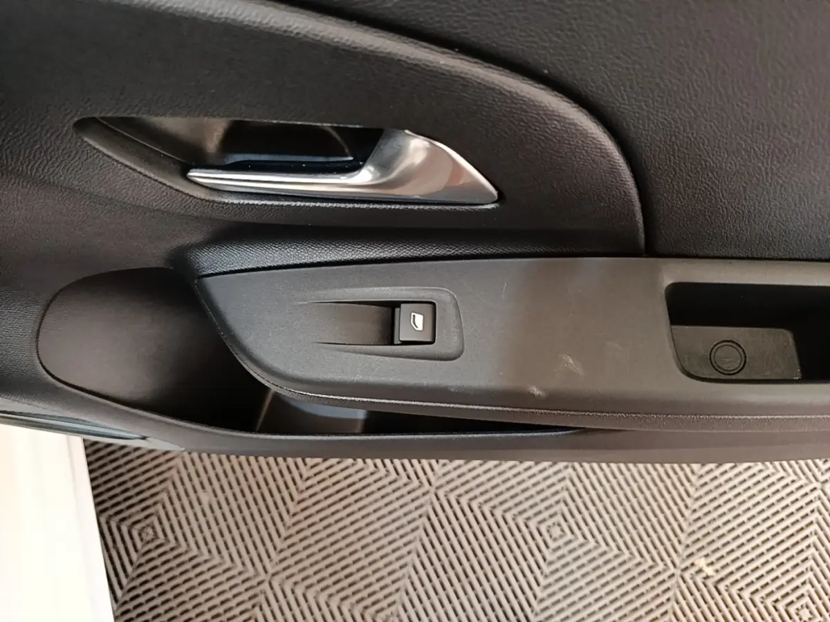 Gros plan sur la poignée intérieure et le bouton de verrouillage de la porte côté conducteur d'une Opel Corsa blanche.