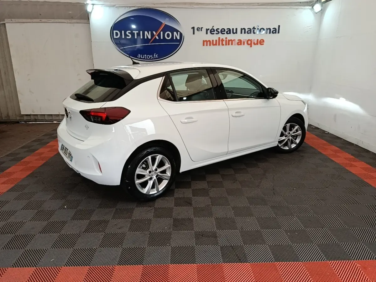 Opel Corsa blanche vue 3/4 arrière droit en intérieur, avec jantes alliage et toit avec spoiler noir.