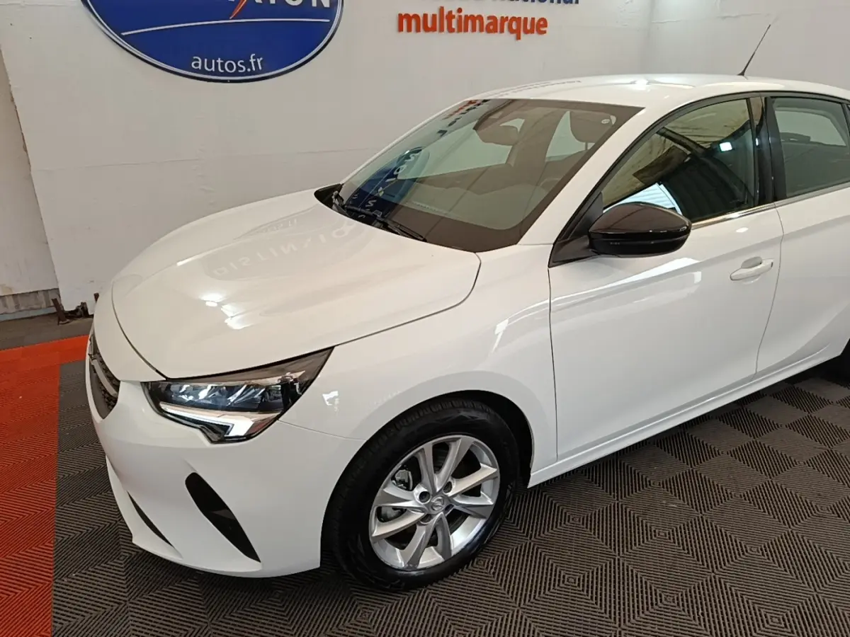 Opel Corsa blanc vue 3/4 avant droit, avec rétroviseurs noirs et jantes alliage argentées.