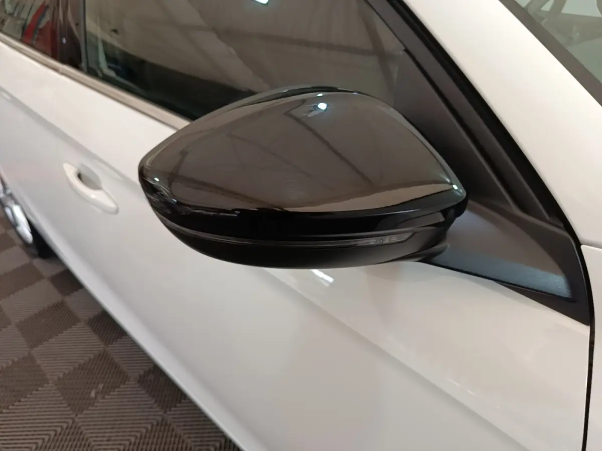 Gros plan sur le rétroviseur noir côté gauche d'une Opel Corsa blanche, avec porte et vitre partiellement visibles.