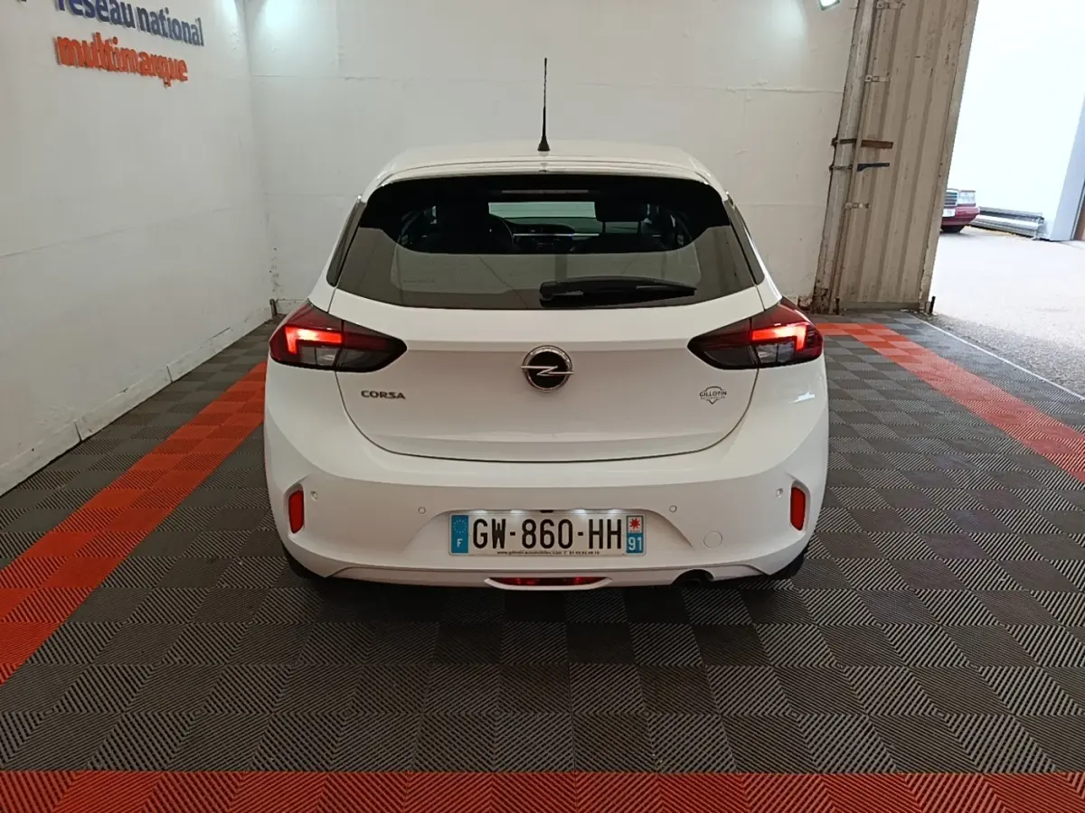 Vue arrière d'une Opel Corsa blanche 2022 avec feux LED allumés, stationnée sur un sol à damier gris et rouge.