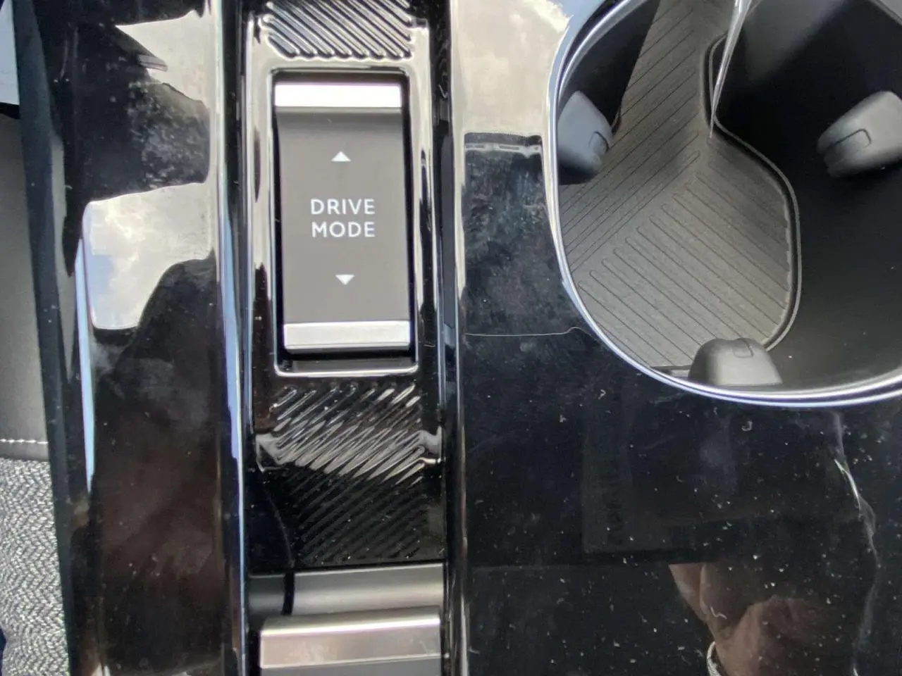 Gros plan sur la console centrale noire brillante de la Citroën C5 X gris platinium, avec bouton Drive Mode et porte-gobelet.