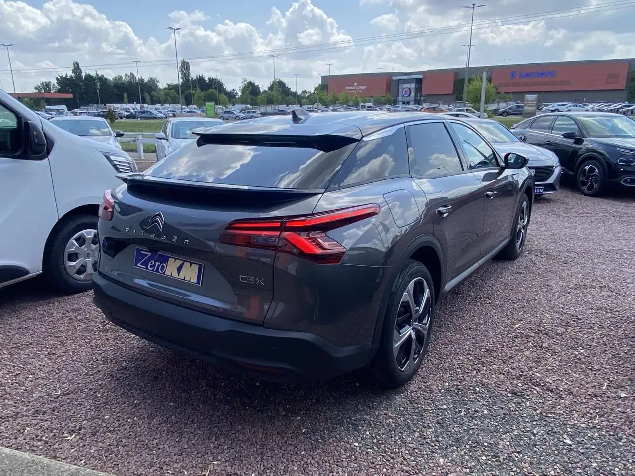 Vue 3/4 arrière droite d'une Citroën C5 X gris platinium avec jantes alliage et vitres surteintées sur parking.