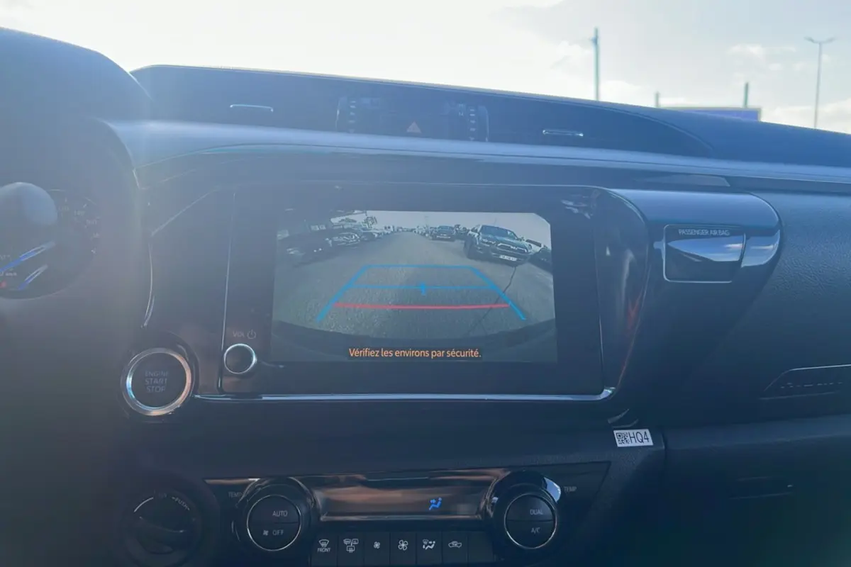 Vue intérieure du tableau de bord du Toyota Hilux 2025 gris atlas, écran affichant la caméra de recul avec consigne de sécurité.