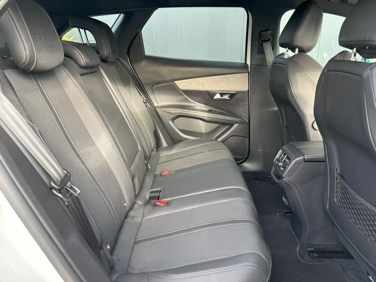 Vue latérale gauche de la banquette arrière noire en tissu et cuir du Peugeot 3008 2024, avec portes et aérateurs visibles.