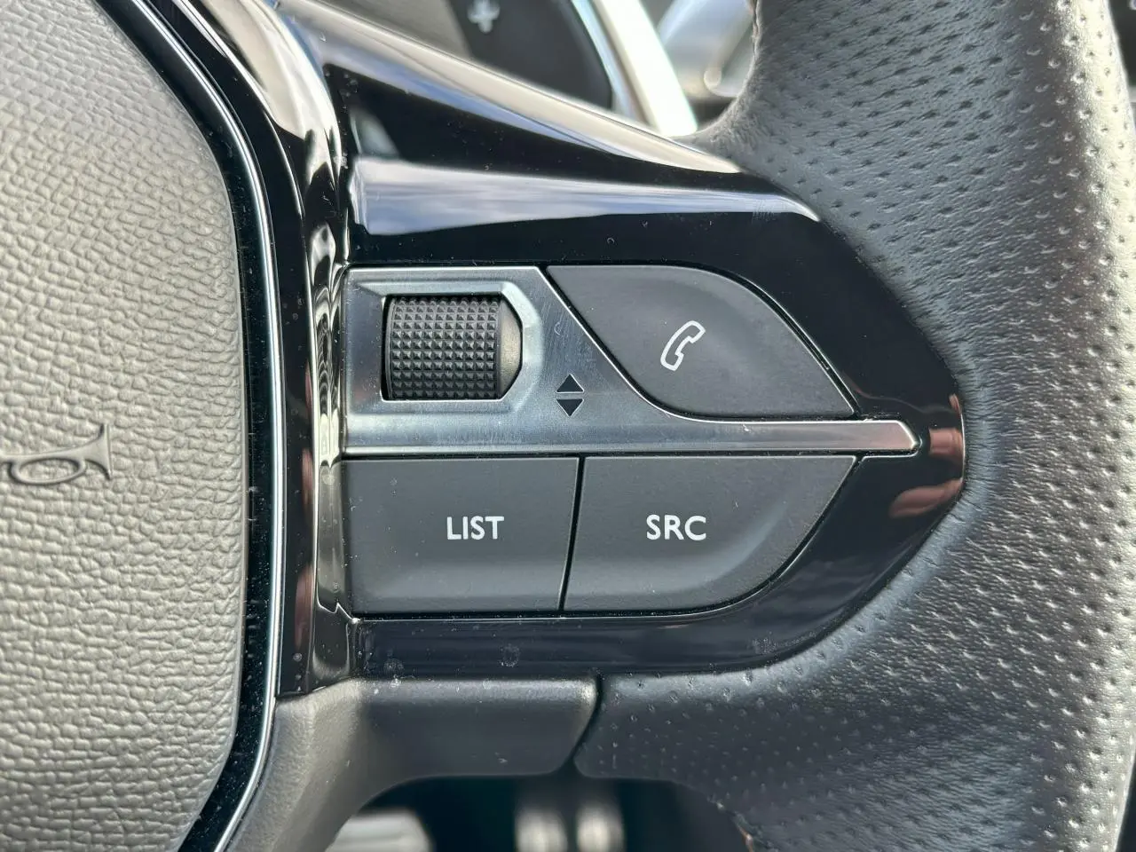 Gros plan sur les commandes gauche du volant cuir perforé du Peugeot 3008 2024, boutons noirs et chrome brillant.