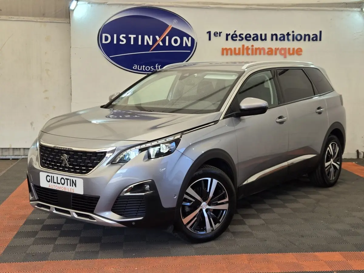Peugeot 5008 gris clair vue 3/4 avant droit, avec jantes alliage bicolores et calandre distinctive noire.
