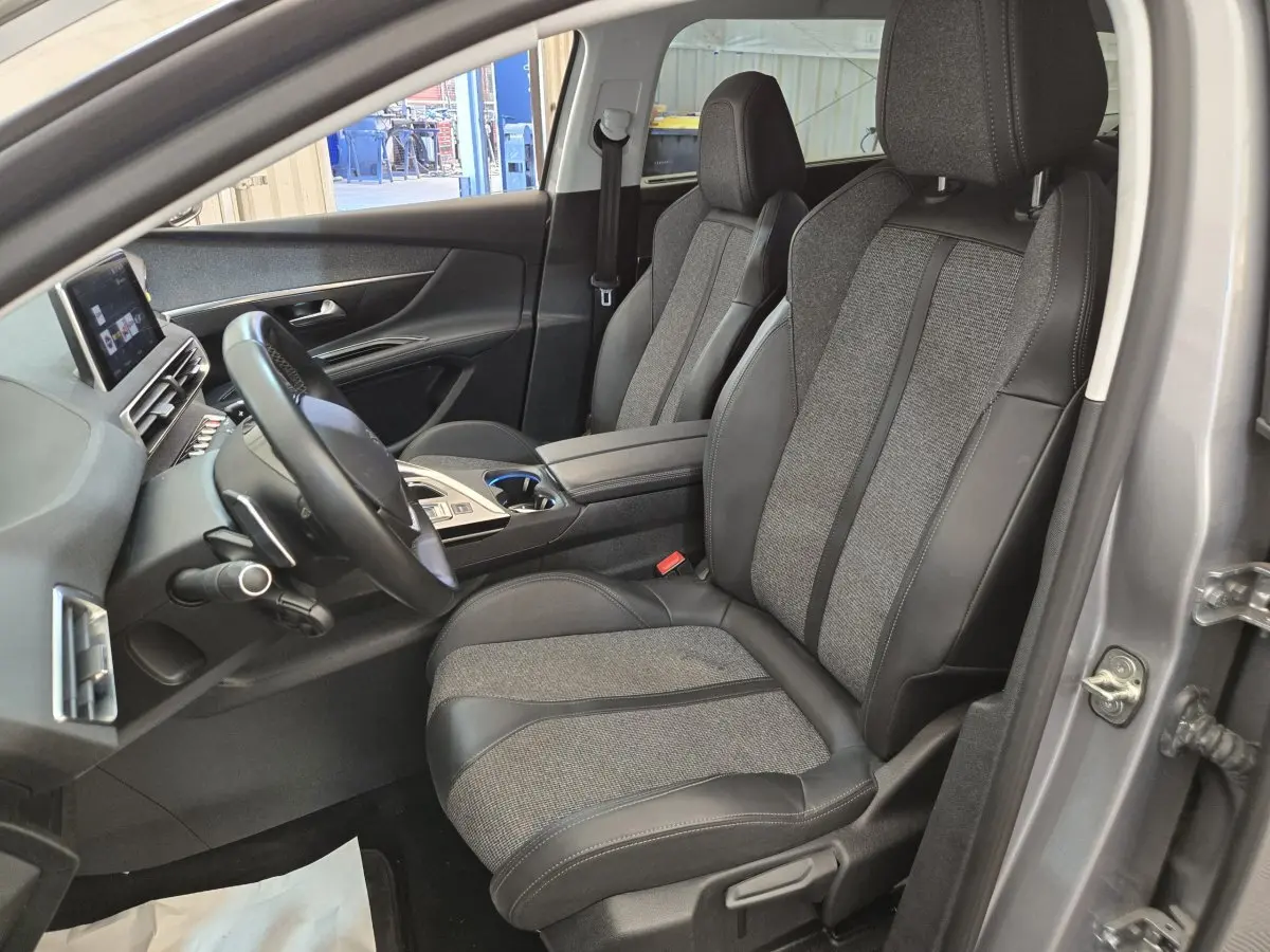 Vue intérieure côté conducteur du Peugeot 5008 gris clair, mettant en valeur les sièges en tissu et cuir ainsi que le tableau de bord digital.