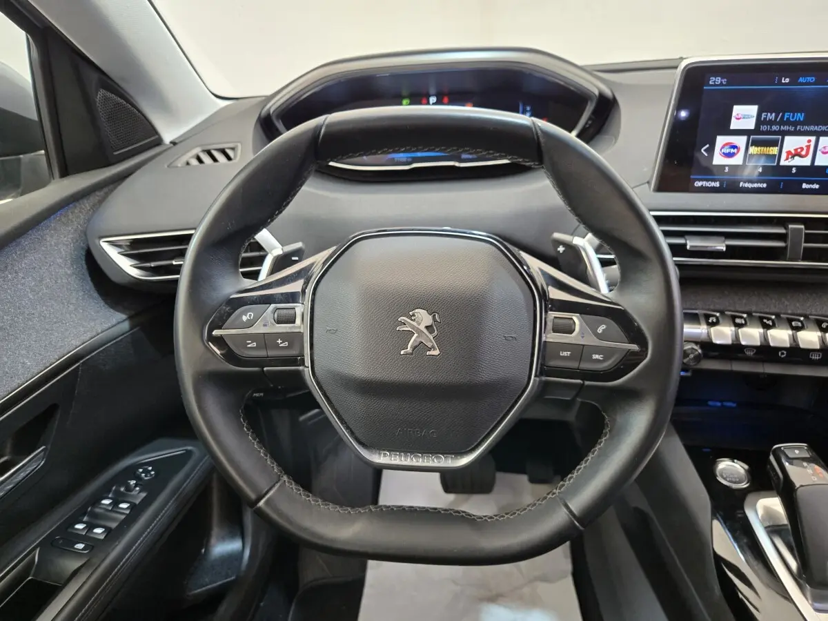 Vue rapprochée du volant cuir noir et du tableau de bord digital d’un Peugeot 5008 gris clair, intérieur moderne et épuré.