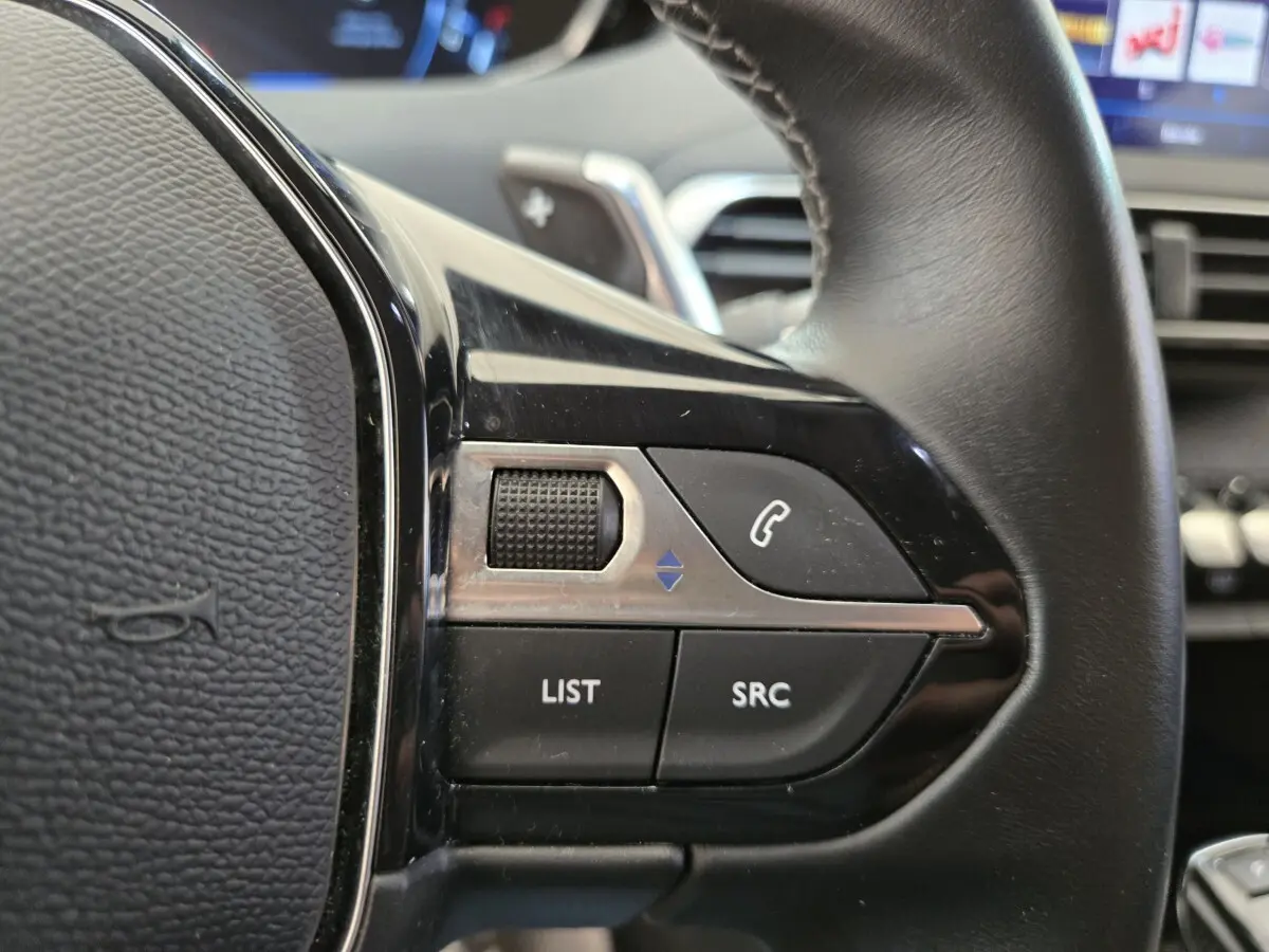 Gros plan sur les commandes noires du volant côté gauche du Peugeot 5008 gris clair, avec boutons LIST et SRC visibles.