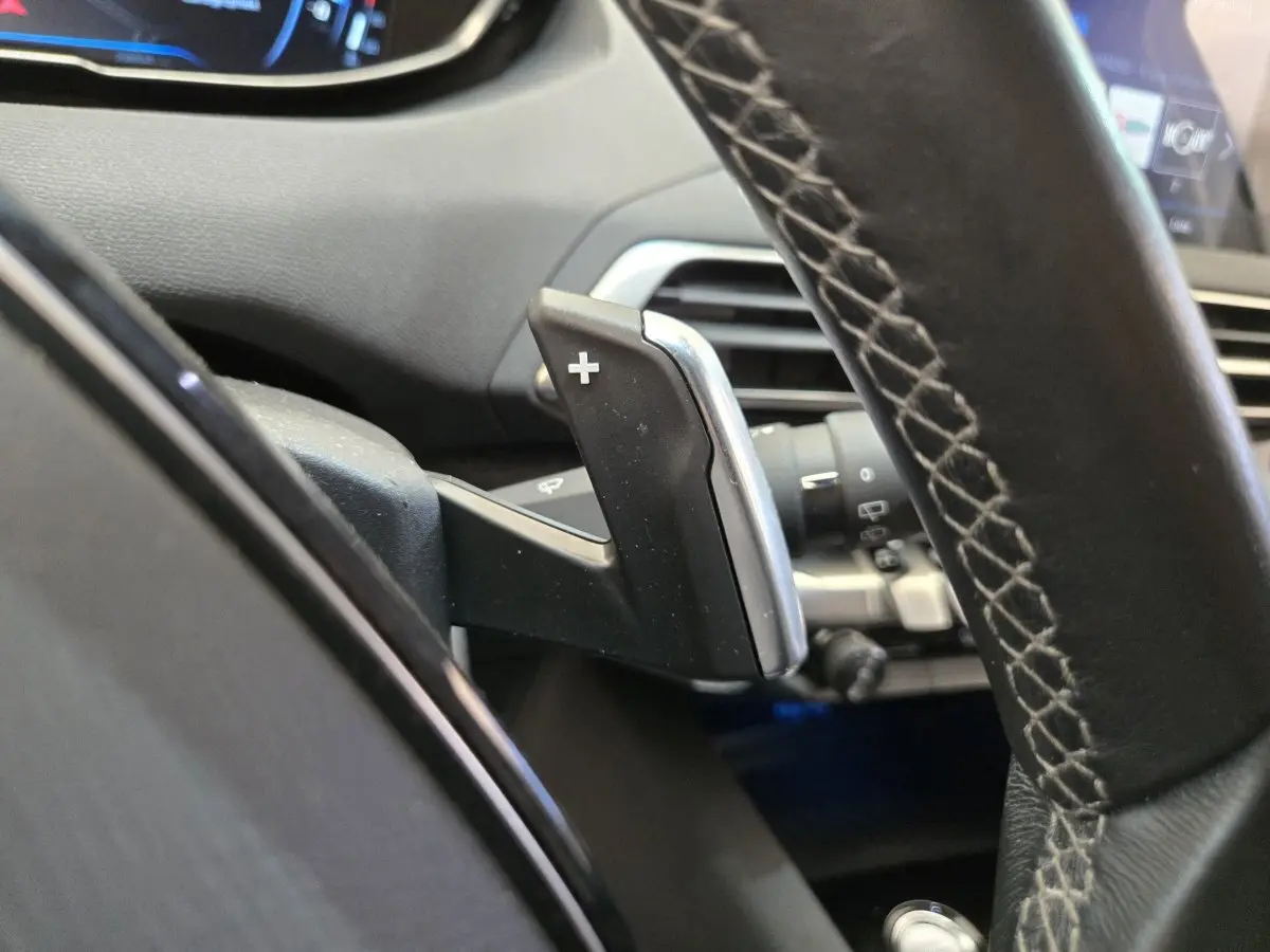 Gros plan sur la palette de changement de vitesse + au volant cuir du Peugeot 5008 gris clair, intérieur moderne et digital.