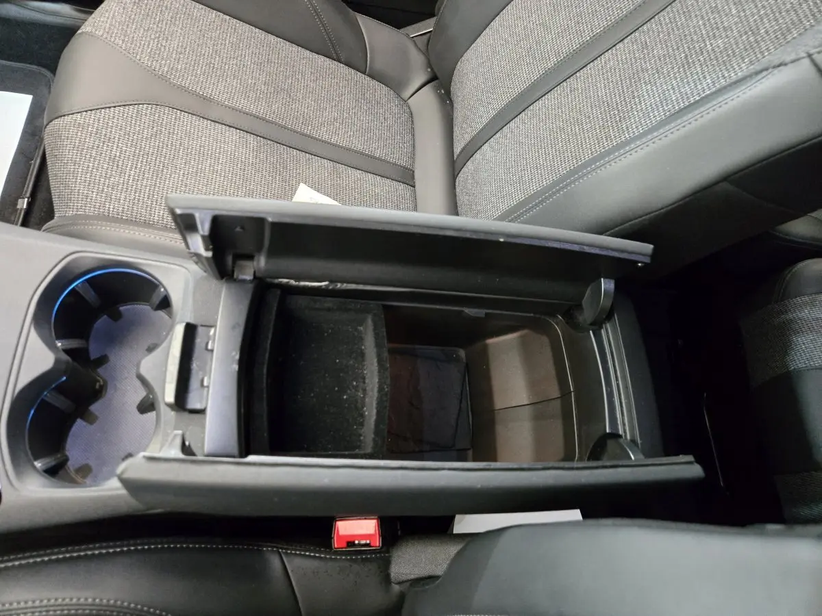 Vue plongeante sur la console centrale ouverte du Peugeot 5008 gris clair, avec porte-gobelets et sièges tissu et cuir.