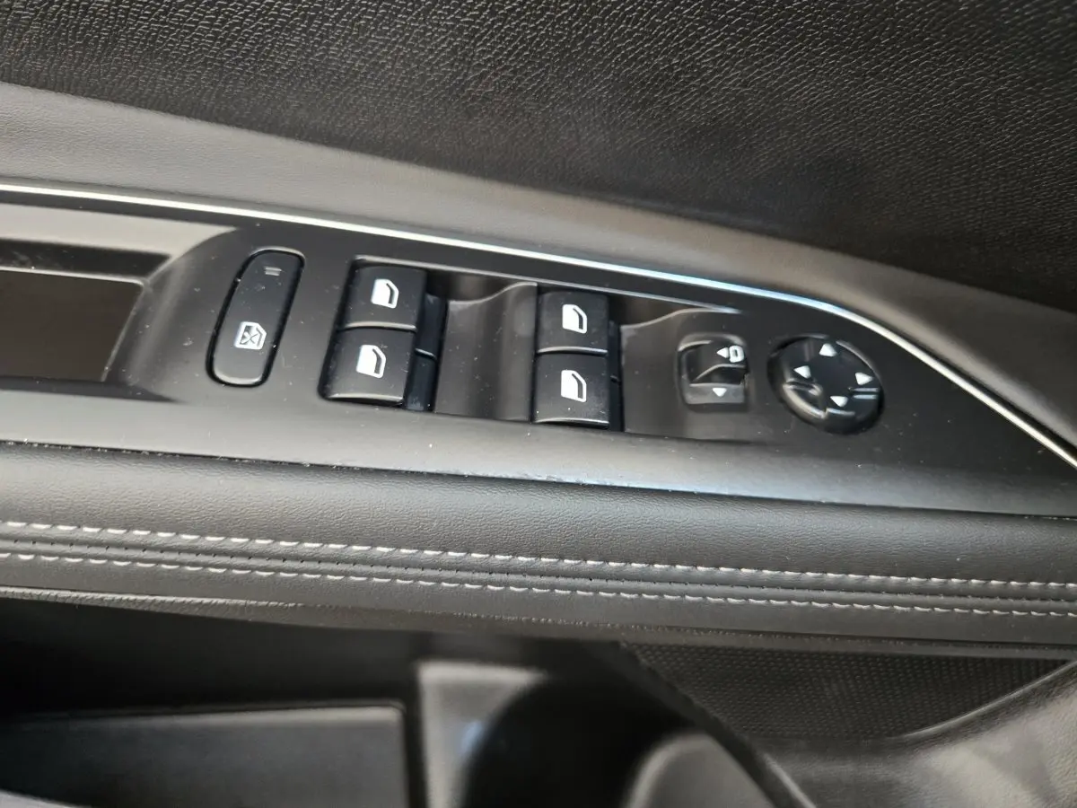 Détail des commandes de lève-vitres et réglage des rétroviseurs sur la porte intérieure noire du Peugeot 5008.