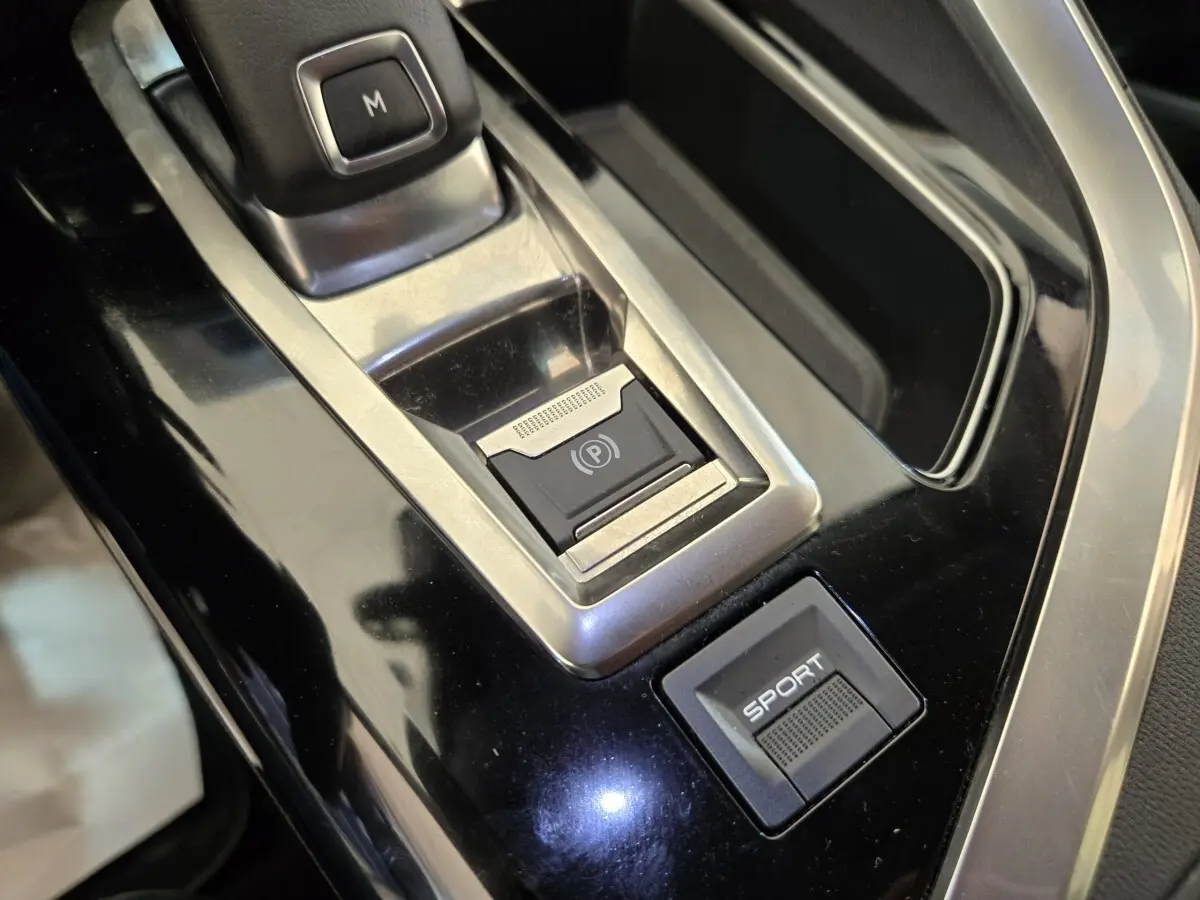 Gros plan sur la console centrale noire brillante du Peugeot 5008 avec bouton frein électrique et mode Sport.