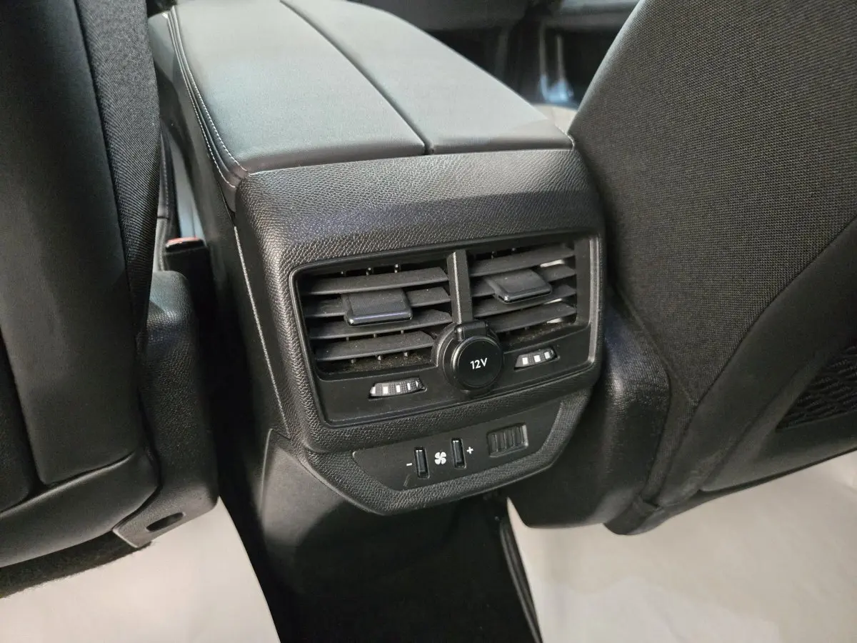 Vue rapprochée des commandes de ventilation arrière et prise 12V sur console centrale d’un Peugeot 5008 gris clair.