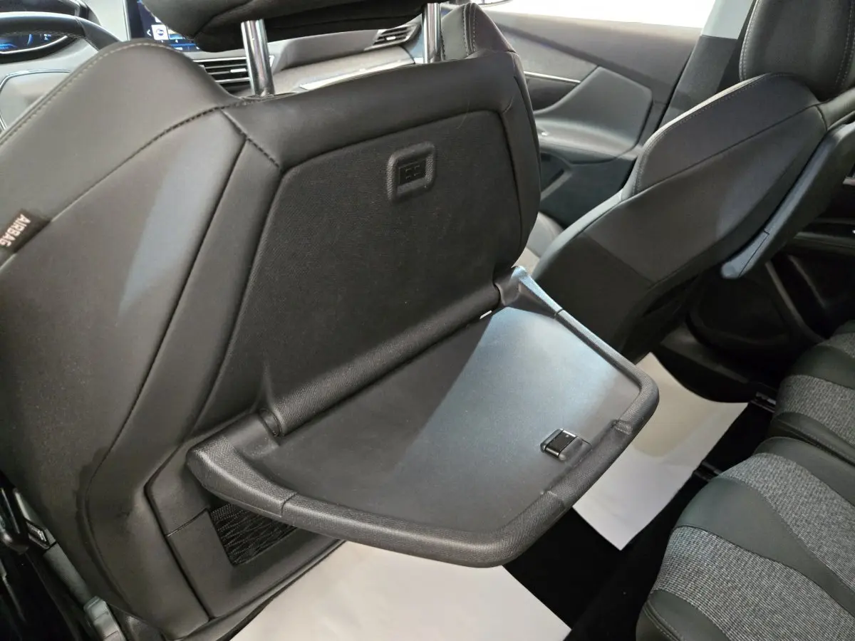 Vue intérieure arrière du Peugeot 5008 gris clair, tablette rabattable sur le dossier du siège avant droit visible.